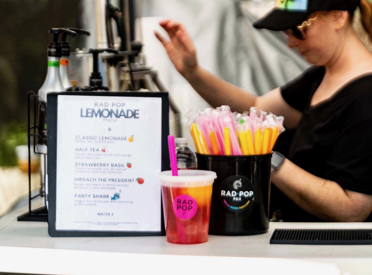 Rad Pop lemonade menu beside a pink drink and a bucket of colorful straws